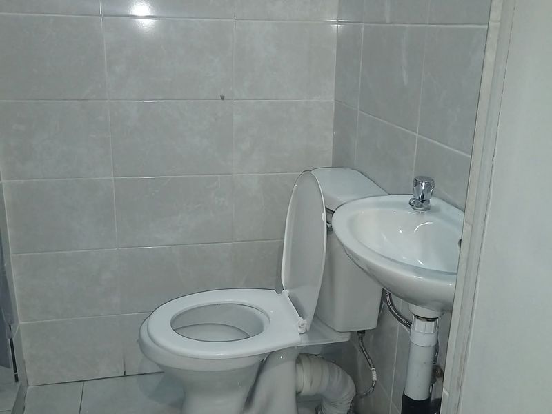 A compact bathroom featuring a standard toilet and pedestal basin with neutral ceramic wall and floor tiling.
