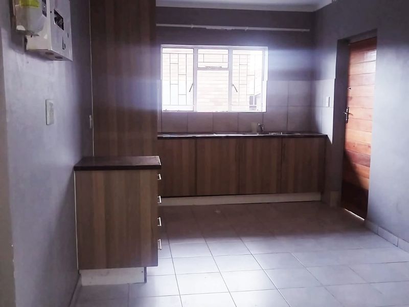 A functional, empty kitchen featuring laminate cabinetry, tiled flooring, and a window with security bars, offering a clean slate for potential updates.