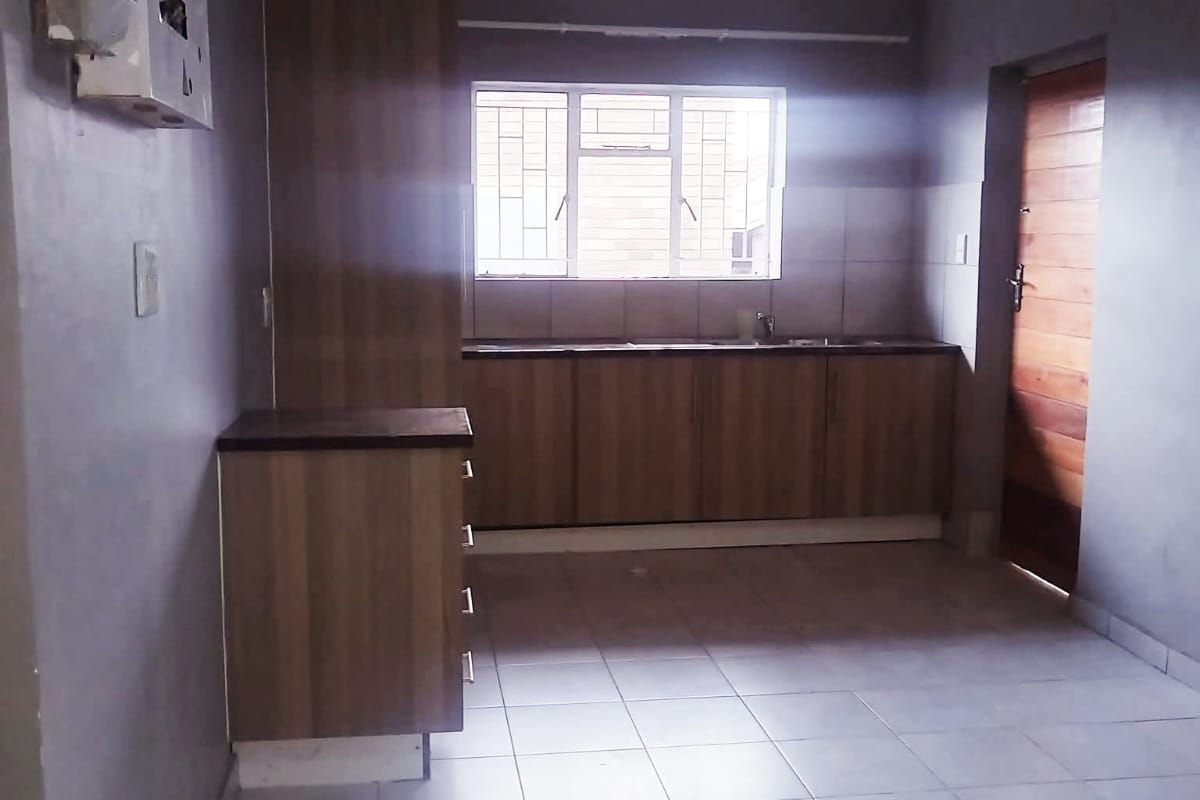 A functional, empty kitchen featuring laminate cabinetry, tiled flooring, and a window with security bars, offering a clean slate for potential updates.