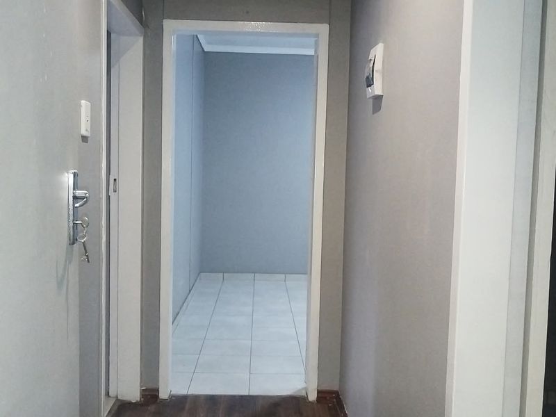 A functional hallway featuring a transition between laminate and tiled flooring, connecting multiple interior spaces with neutral wall finishes.