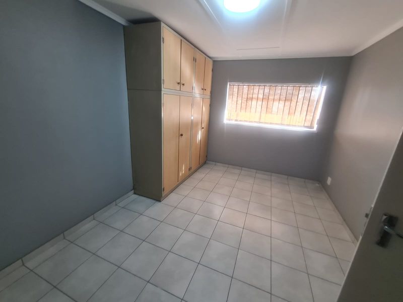 A vacant bedroom featuring tiled flooring, grey painted walls, and built-in wooden cupboards with overhead storage.
