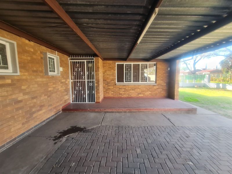 Front exterior view featuring a covered carport, brick facade, paved driveway, and a secure entrance with security gate and bars.