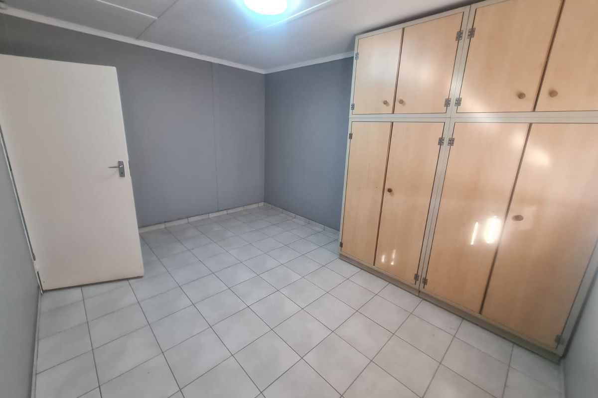 An empty bedroom featuring tiled flooring and extensive built-in wooden cupboards, providing ample storage space.