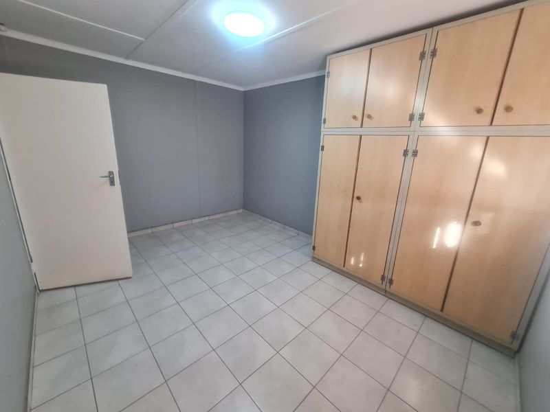 An empty bedroom featuring tiled flooring and extensive built-in wooden cupboards, providing ample storage space.