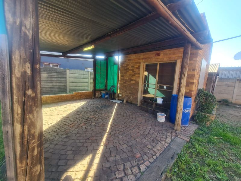 A covered outdoor patio area featuring brick paving, timber support posts, and a corrugated metal roof, providing a functional space for outdoor living.