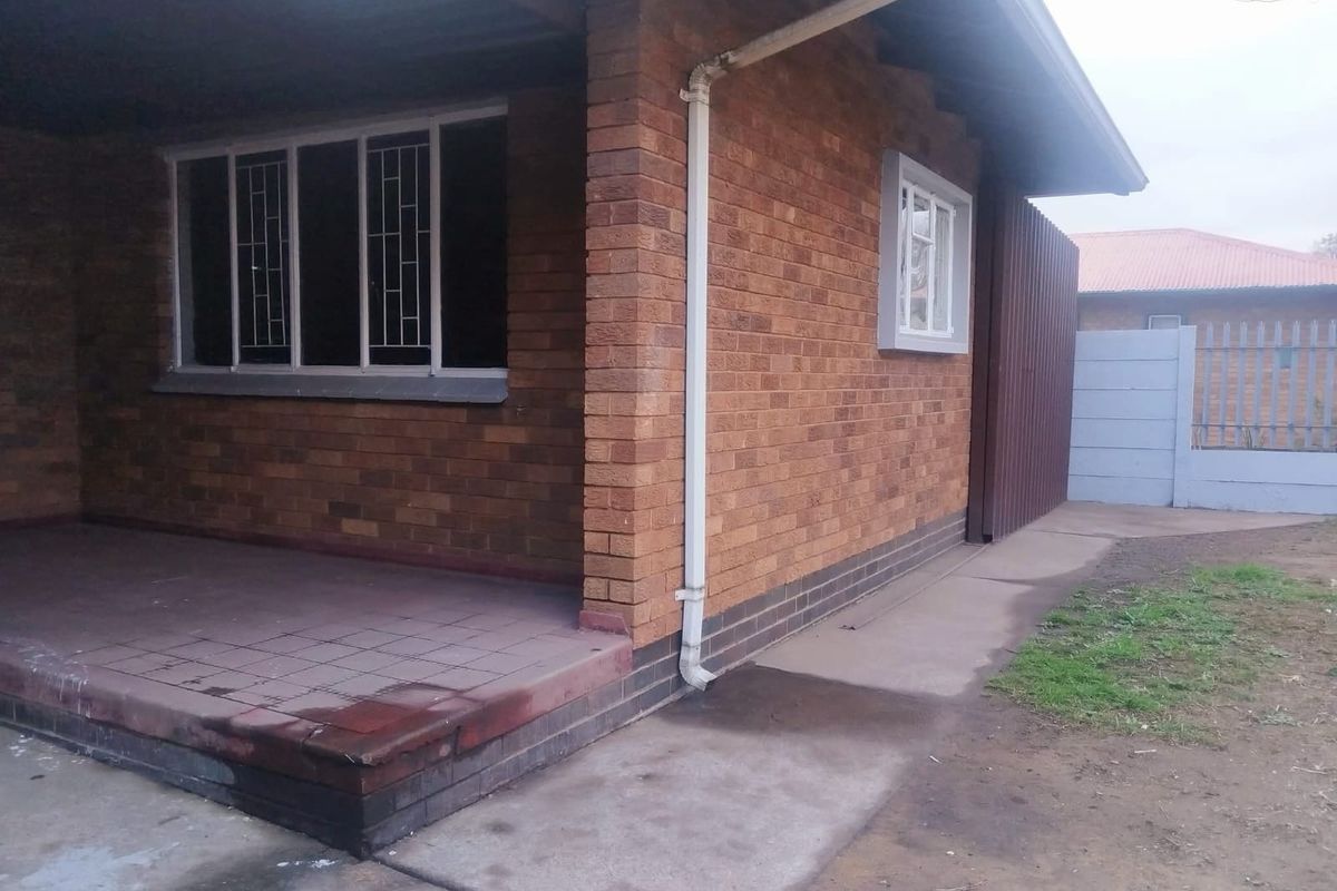 A view of the rear exterior featuring a brick facade, a tiled patio area, and a concrete walkway leading to the boundary wall.