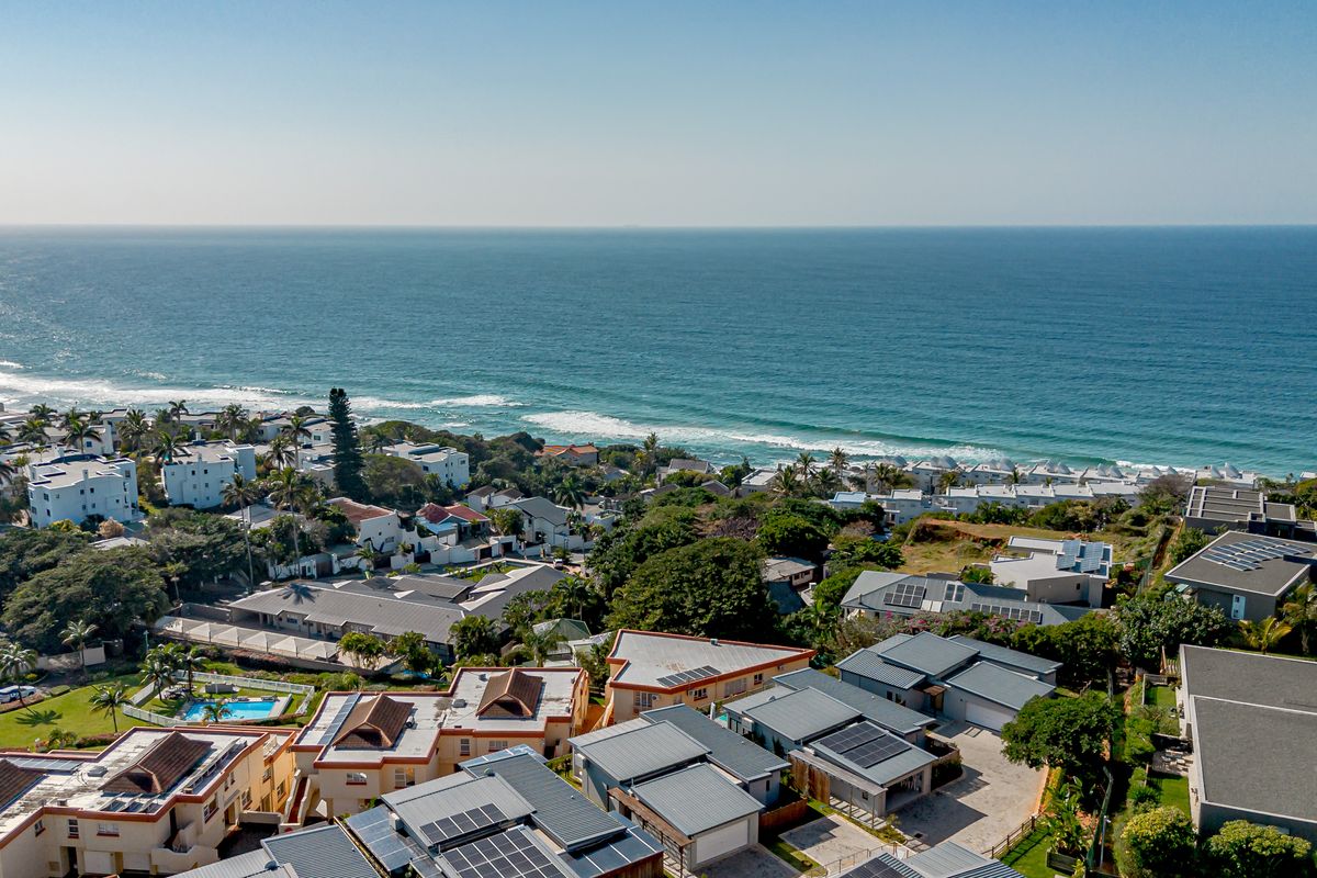 An elevated aerial view of a coastal residential estate featuring multiple homes with solar panels, tiled roofs, and proximity to the ocean.