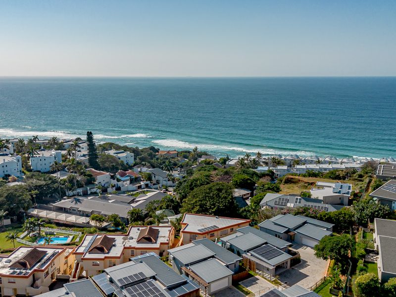 An elevated aerial view of a coastal residential estate featuring multiple homes with solar panels, tiled roofs, and proximity to the ocean.