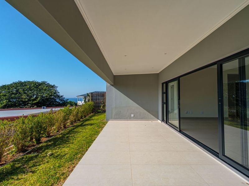 A spacious, modern covered patio featuring large format floor tiles, recessed lighting, and expansive sliding glass doors leading into the home.