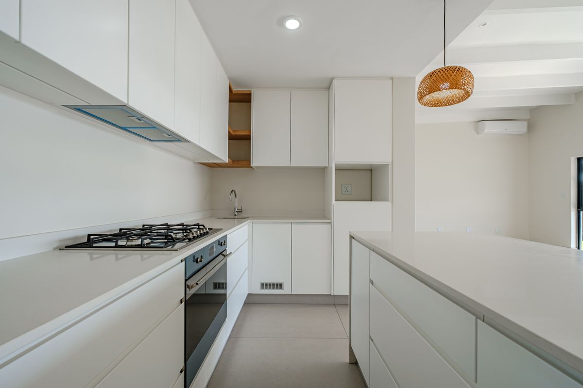 Modern, minimalist kitchen featuring white cabinetry, quartz countertops, integrated gas hob, built-in oven, and a functional kitchen island in an open-plan layout.