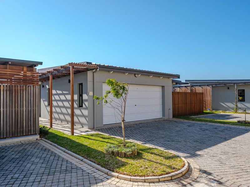 A modern residential garage exterior featuring a paved driveway, timber pergola, and well-maintained timber fencing in a clean, contemporary estate setting.