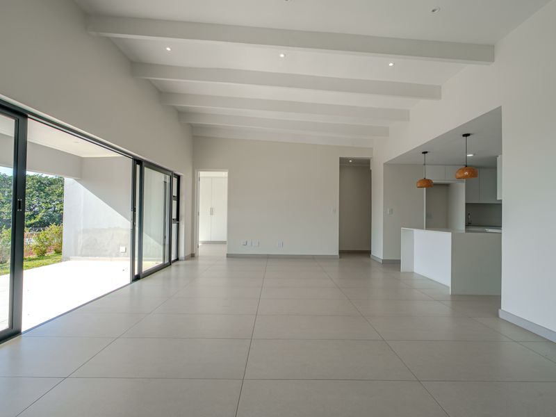 Spacious open-plan living area featuring large format floor tiles, exposed ceiling beams, and seamless flow to the outdoor patio through expansive sliding glass doors.