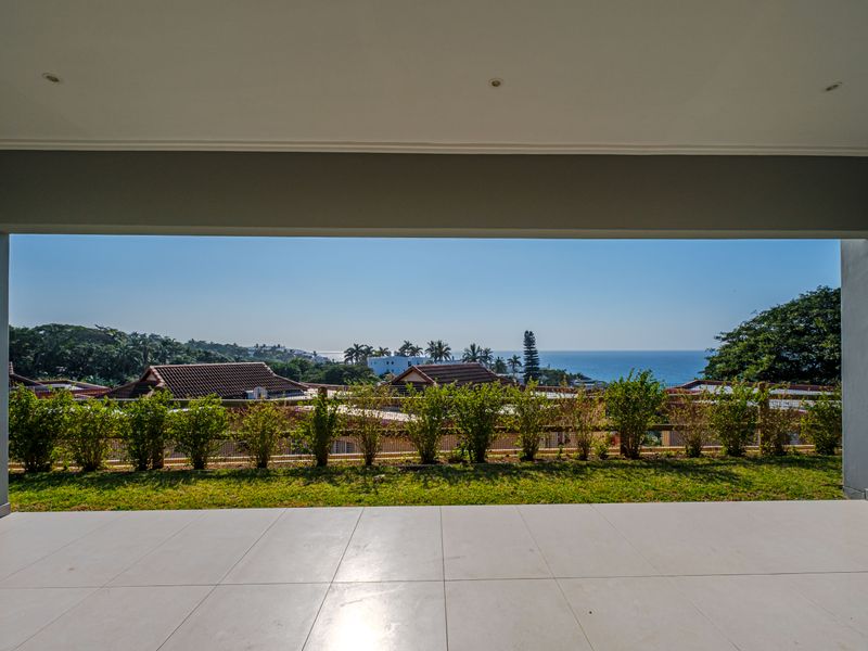 A spacious covered patio featuring clean tiled flooring and recessed lighting, offering an expansive view of the surrounding landscape and ocean.