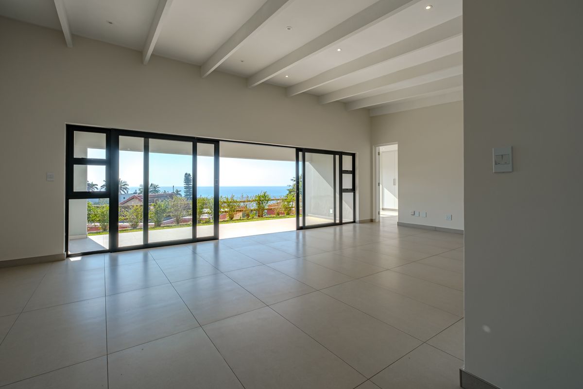 Spacious, light-filled living area featuring exposed ceiling beams, large format floor tiles, and expansive sliding glass doors opening to a scenic outdoor view.