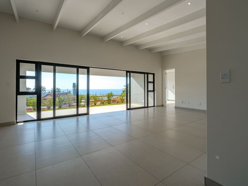 Spacious, light-filled living area featuring exposed ceiling beams, large format floor tiles, and expansive sliding glass doors opening to a scenic outdoor view.