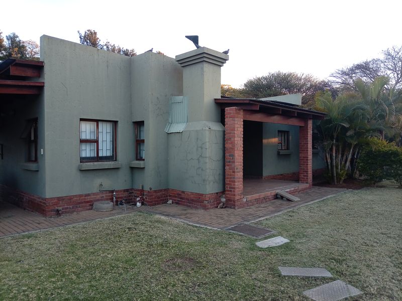 Rear view of a townhouse featuring a covered patio, brick chimney, and paved garden area with visible exterior wall cracking.