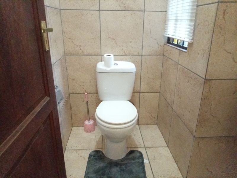 A compact bathroom featuring neutral ceramic wall and floor tiles, a standard toilet, and a window with a fitted blind.