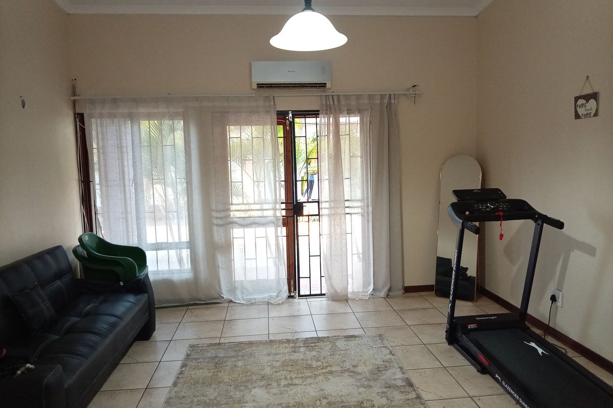 A living room featuring tiled flooring, a split-system air conditioner, and a sliding glass door with a security gate leading to the exterior.