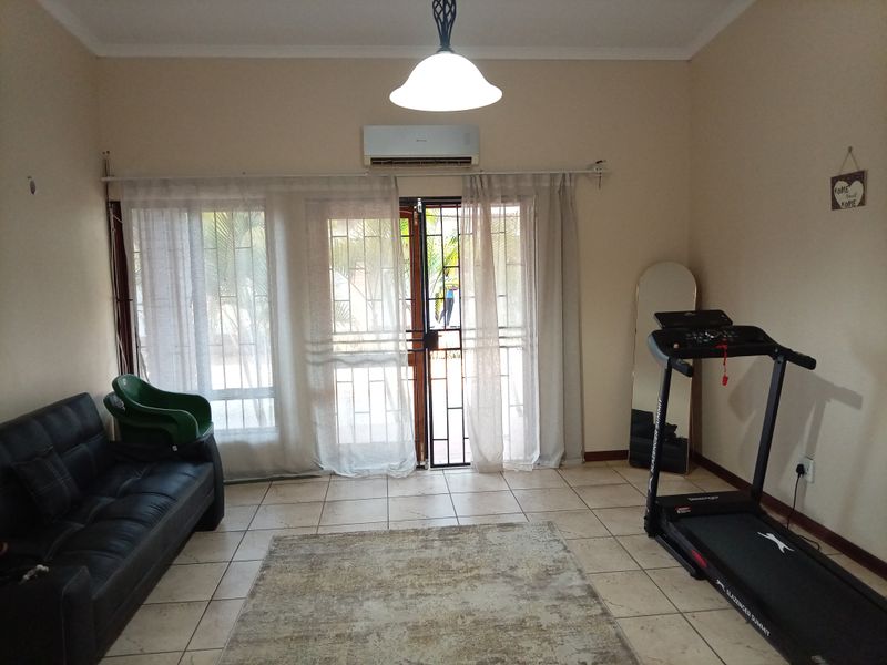 A living room featuring tiled flooring, a split-system air conditioner, and a sliding glass door with a security gate leading to the exterior.