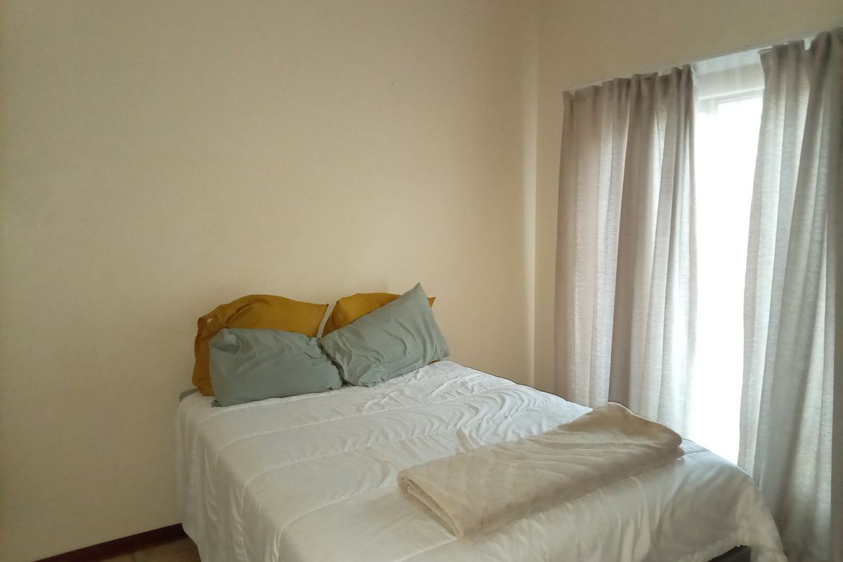 A simple bedroom featuring tiled flooring and natural light provided by a window with installed curtain tracks.