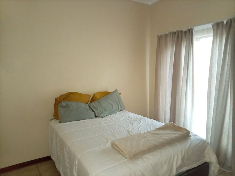 A simple bedroom featuring tiled flooring and natural light provided by a window with installed curtain tracks.