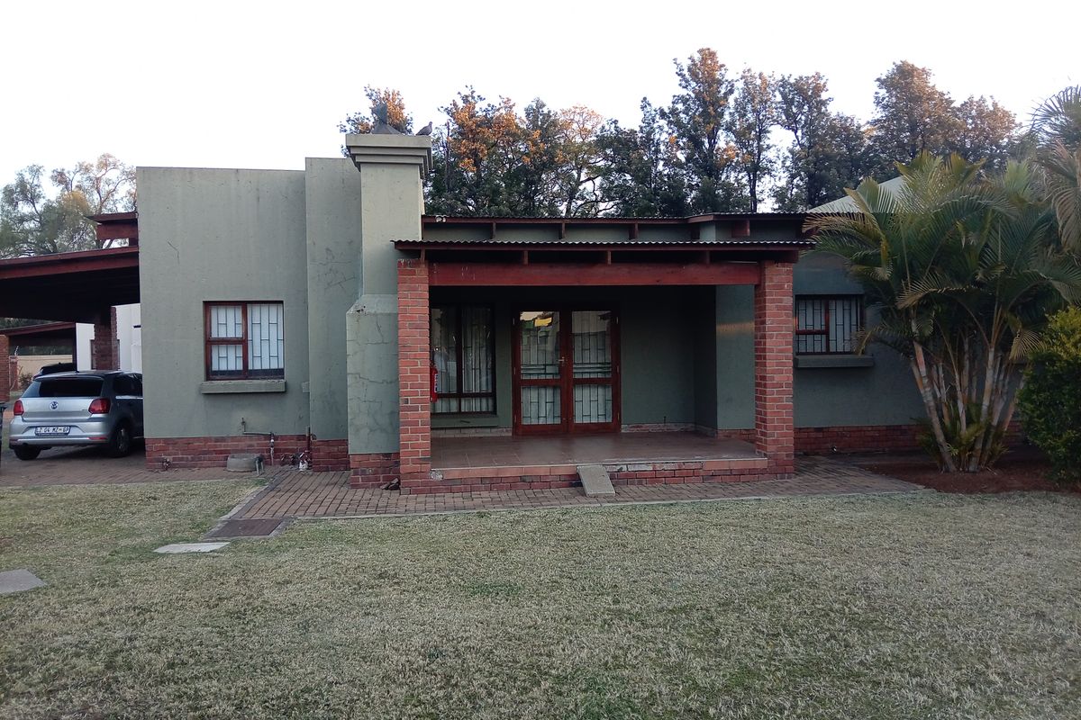 Rear view of the townhouse featuring a covered patio with brick pillars, a chimney, and security bars on the windows, set against a garden.