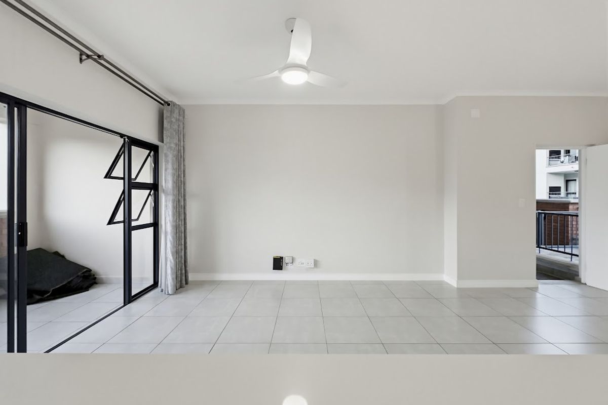 A bright, empty living room featuring neutral tiled flooring, a modern ceiling fan, and large sliding glass doors leading to an outdoor area.