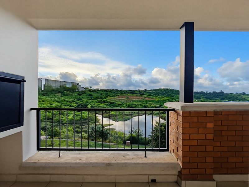 A covered balcony featuring a metal balustrade and brick pillar, offering scenic views of the surrounding landscape and water feature.