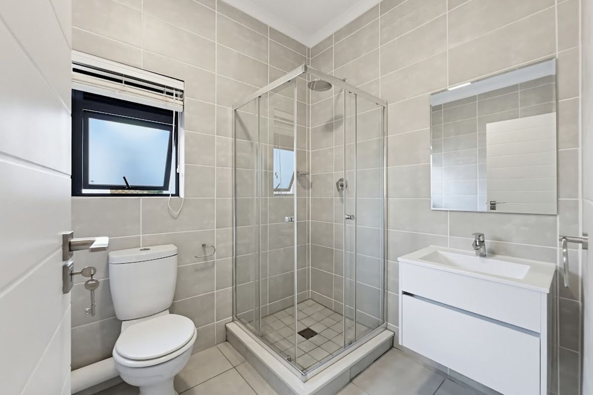 A modern, well-maintained bathroom featuring a glass shower enclosure, wall-mounted vanity with basin, and neutral floor-to-ceiling tiling.