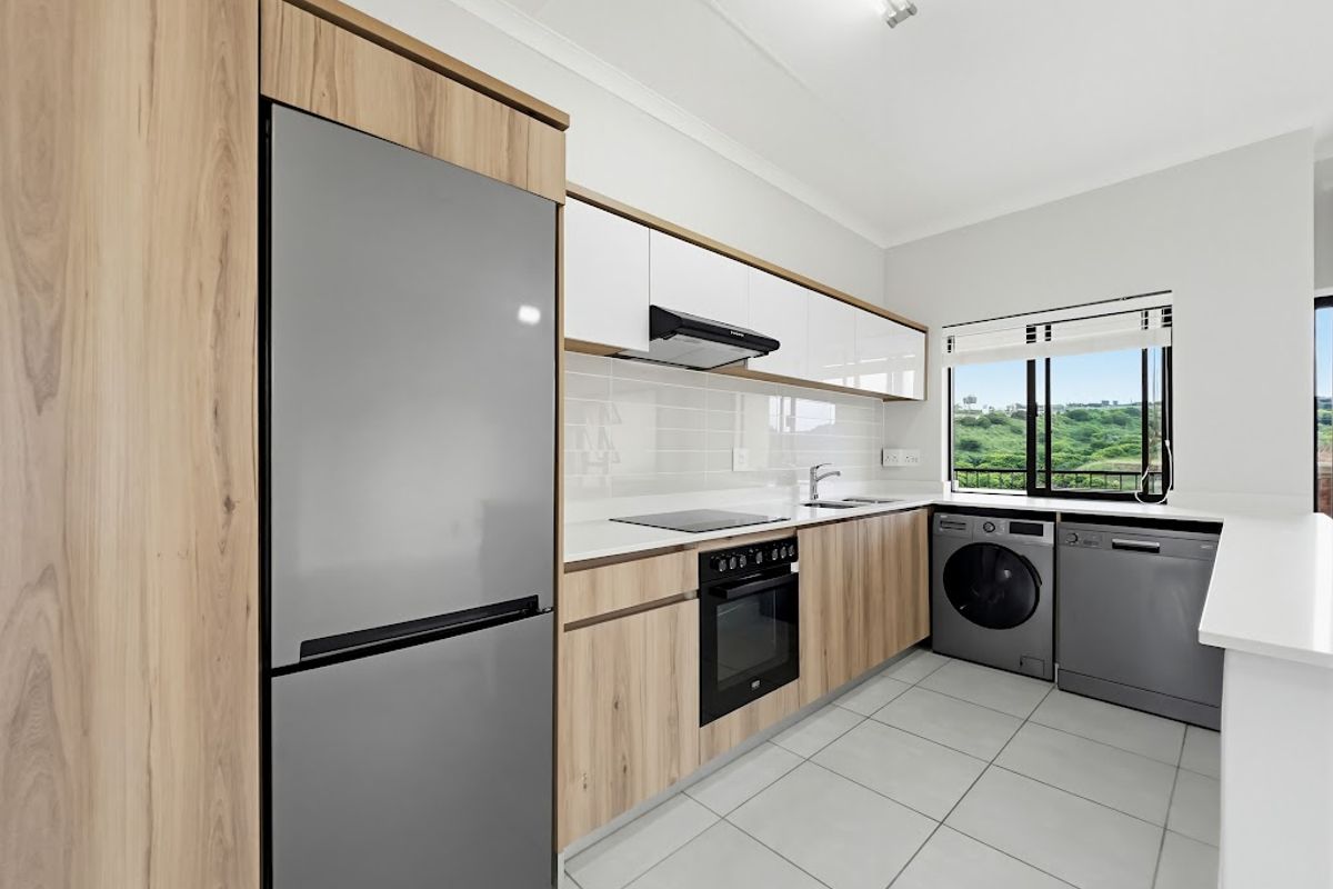 Modern kitchen featuring light wood-grain cabinetry, white countertops, integrated appliances, and tiled flooring with a view through the window.