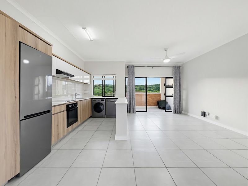 Modern open-plan kitchen and living area featuring light wood cabinetry, tiled floors, and direct access to a private balcony with scenic views.