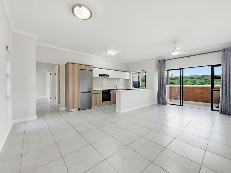 Spacious open-plan living area featuring a modern kitchen with built-in appliances, tiled flooring, and direct access to a private balcony with scenic views.