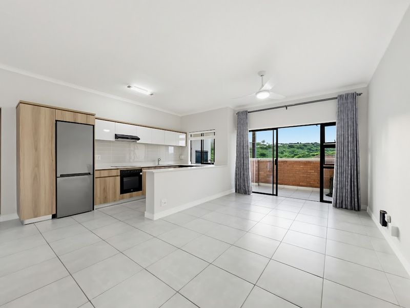 Modern open-plan kitchen and living area featuring sleek cabinetry, built-in appliances, tiled floors, and direct access to a private balcony with scenic views.