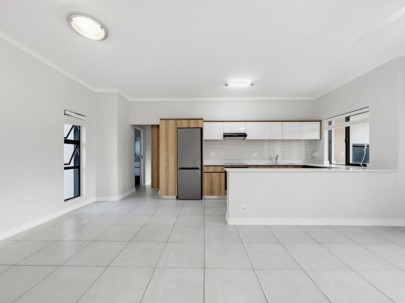 Modern open-plan kitchen featuring sleek cabinetry, tiled flooring, and a functional island, offering a clean and bright space for living and dining.