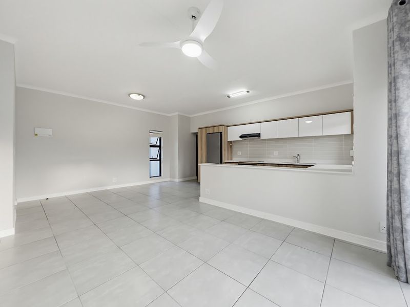 A bright, modern open-plan living and kitchen area featuring neutral tiled flooring, contemporary cabinetry, and a ceiling fan in a clean, well-maintained space.