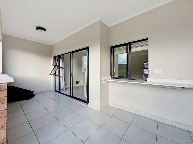 A clean, covered balcony featuring tiled flooring, a built-in serving counter, and sliding glass doors leading into the apartment interior.