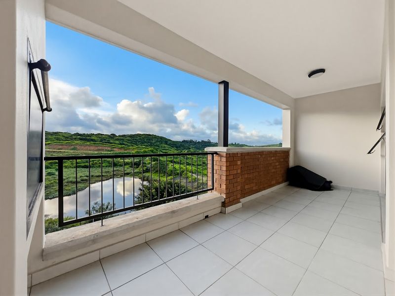 A spacious covered balcony featuring tiled flooring, a brick and metal balustrade, and scenic views of the surrounding landscape and water.