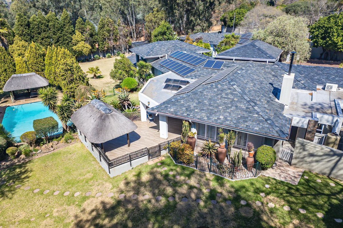 Aerial view of a residential property featuring a large tiled roof with solar panels, a swimming pool, and a thatched outdoor entertainment area.