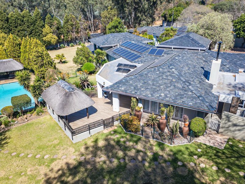 Aerial view of a residential property featuring a large tiled roof with solar panels, a swimming pool, and a thatched outdoor entertainment area.