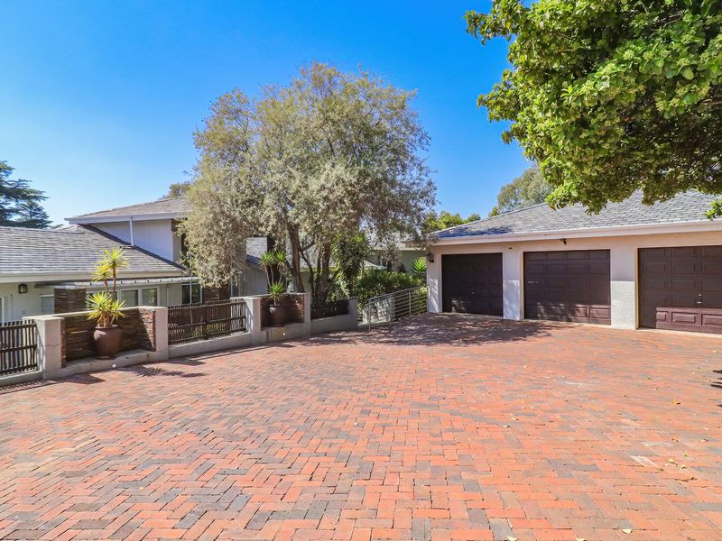 Front view of the property featuring a spacious brick-paved driveway leading to a triple garage and a well-maintained exterior facade.