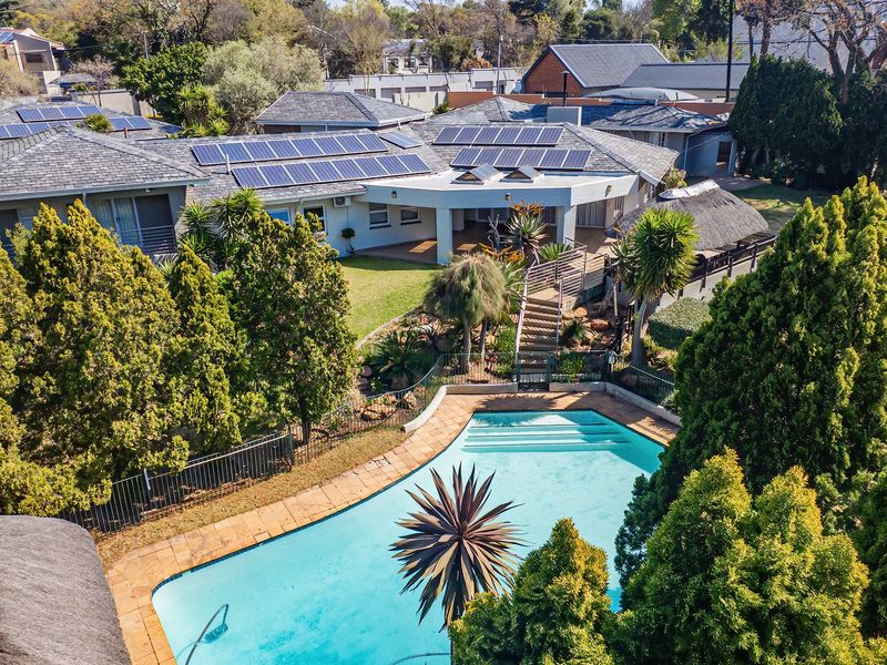 Aerial view of a residential property featuring a swimming pool, landscaped garden, and extensive roof-mounted solar panel installation.