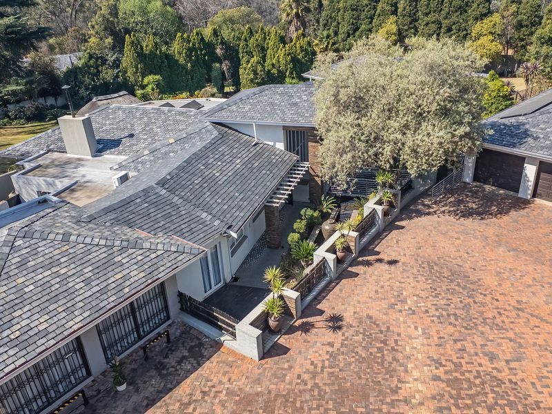 Aerial view of the property showcasing the slate roof, extensive brick paved driveway, double garage, and landscaped garden areas.