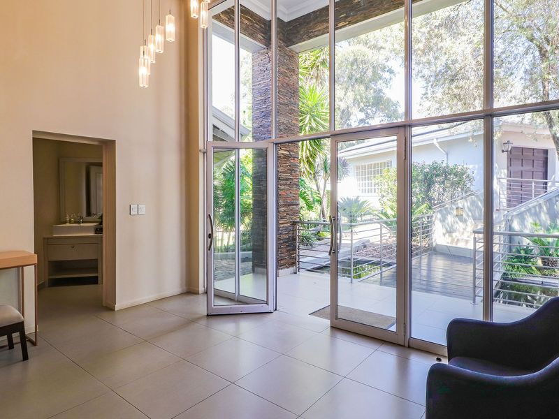 Spacious living area featuring double-volume ceilings, floor-to-ceiling windows, and a striking stone-clad pillar, offering seamless access to the outdoor patio.
