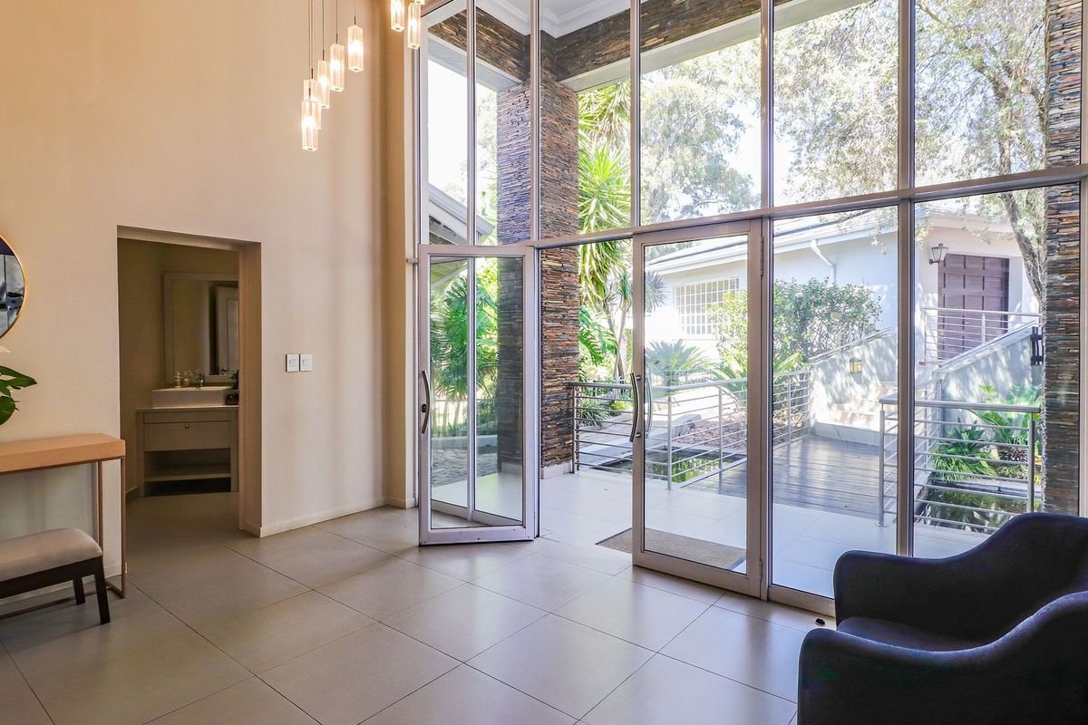 Spacious living area featuring double-volume ceilings, floor-to-ceiling windows, and a striking stone-clad pillar, offering seamless access to the outdoor patio.