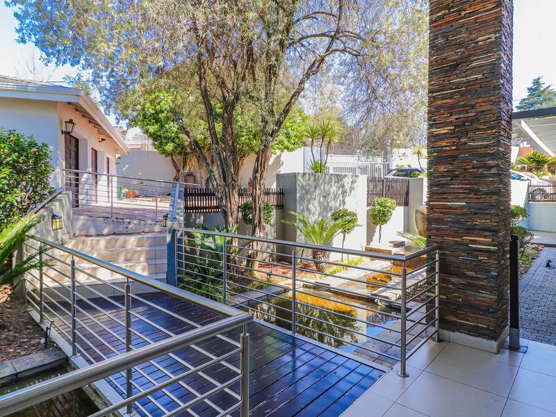 A well-maintained outdoor patio area featuring a timber deck, stainless steel balustrades, a stacked stone pillar, and a tranquil water feature.