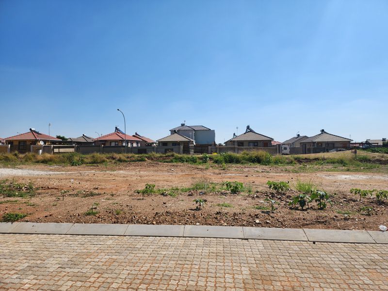 A vacant residential plot featuring a paved driveway and concrete curb, situated in a developed neighborhood with surrounding houses.