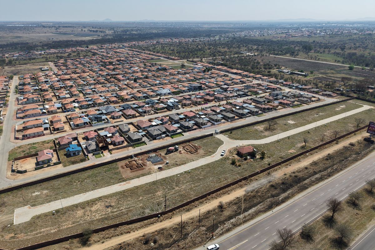 Aerial view of a residential development site featuring perimeter walls, internal access roads, and surrounding infrastructure in a suburban setting.