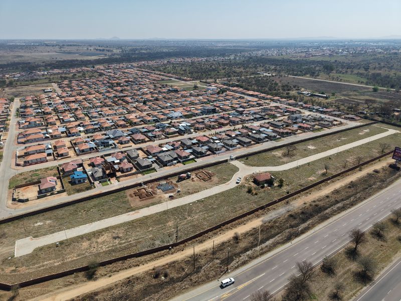 Aerial view of a residential development site featuring perimeter walls, internal access roads, and surrounding infrastructure in a suburban setting.