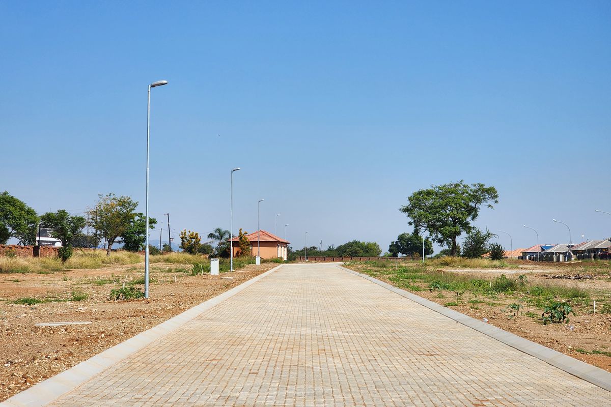 A clear view of a paved residential street within a developing estate, featuring installed street lighting and established kerbing.