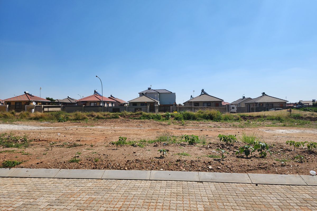 A vacant residential plot featuring a paved driveway and concrete curb, situated in a developed neighborhood with surrounding houses.